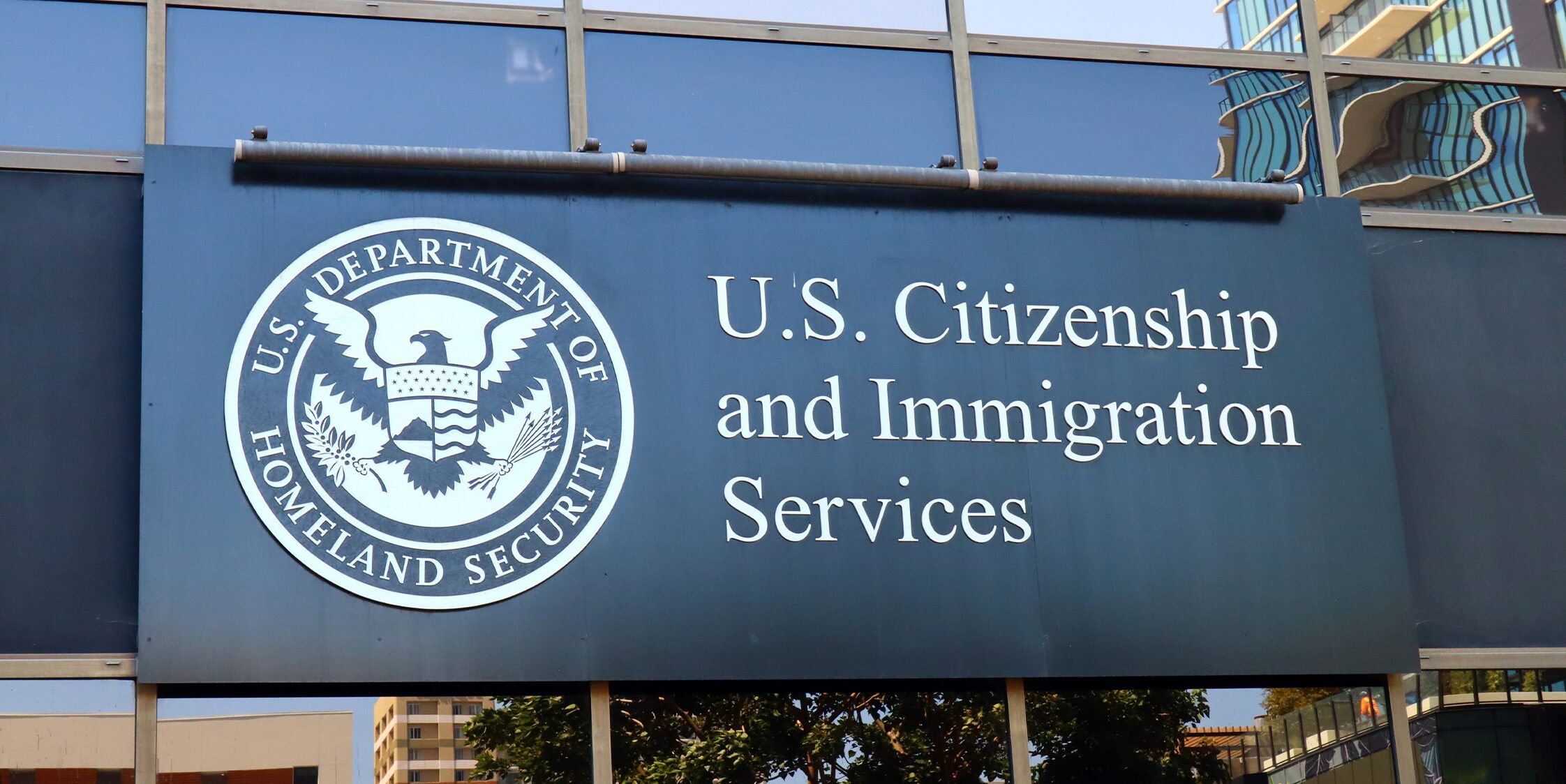 Exterior sign for U.S. Citizenship and Immigration Services featuring the Department of Homeland Security seal on a glass-fronted building.