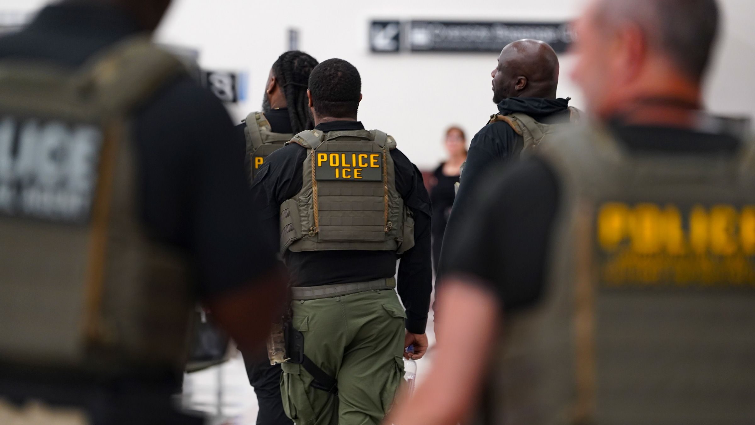 U.S. Immigration and Customs Enforcement (ICE) officers wearing “Police ICE” vests walk through an airport terminal.