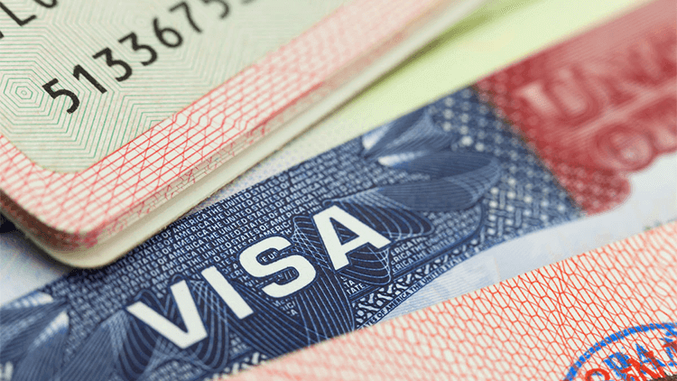 Close-up of a U.S. visa document partially covered by a passport, showing the word “VISA” and security details.