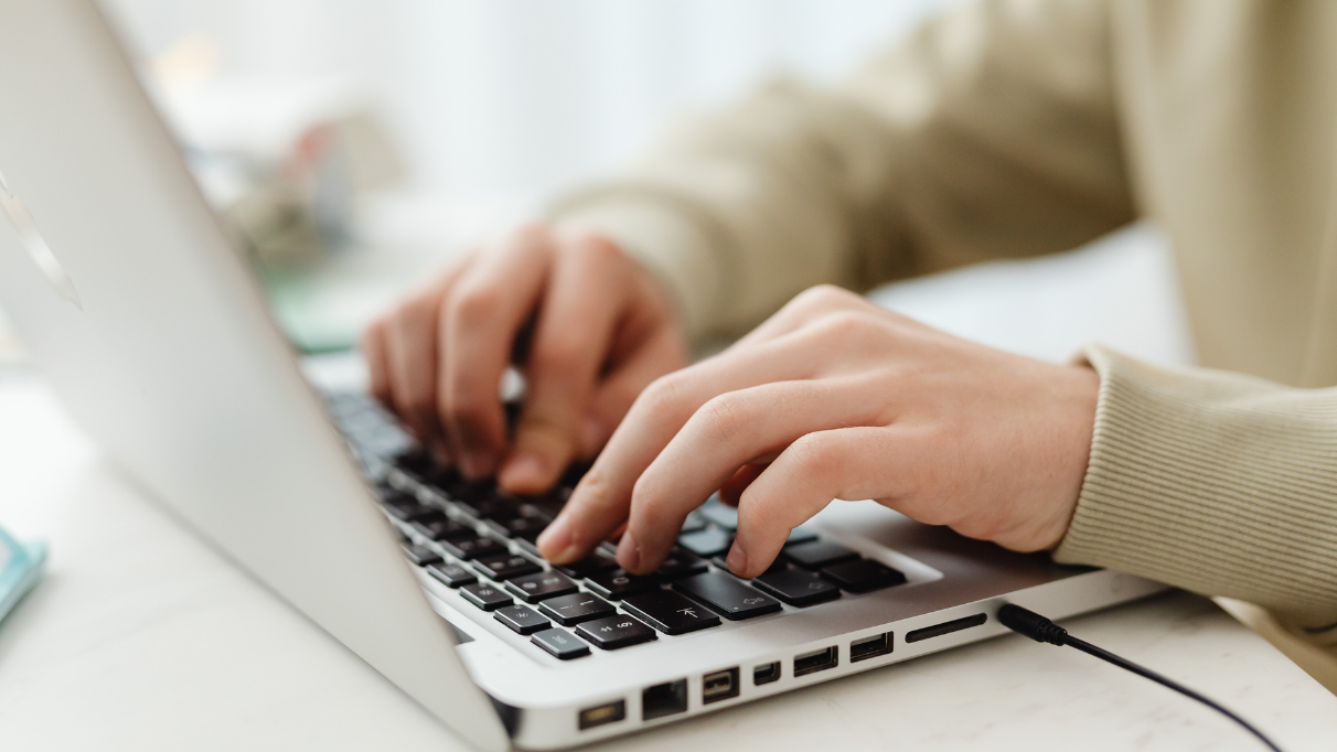 Pessoa digitando em um notebook sobre uma mesa, com as mãos sobre o teclado.