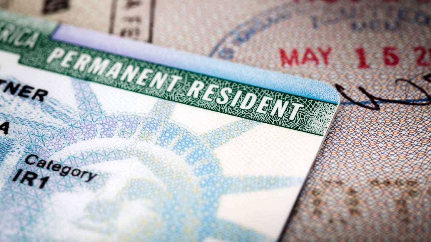 A close-up of a U.S. permanent resident card resting on top of a passport page, with text including "PERMANENT RESIDENT" and "Category IR1" in focus.
