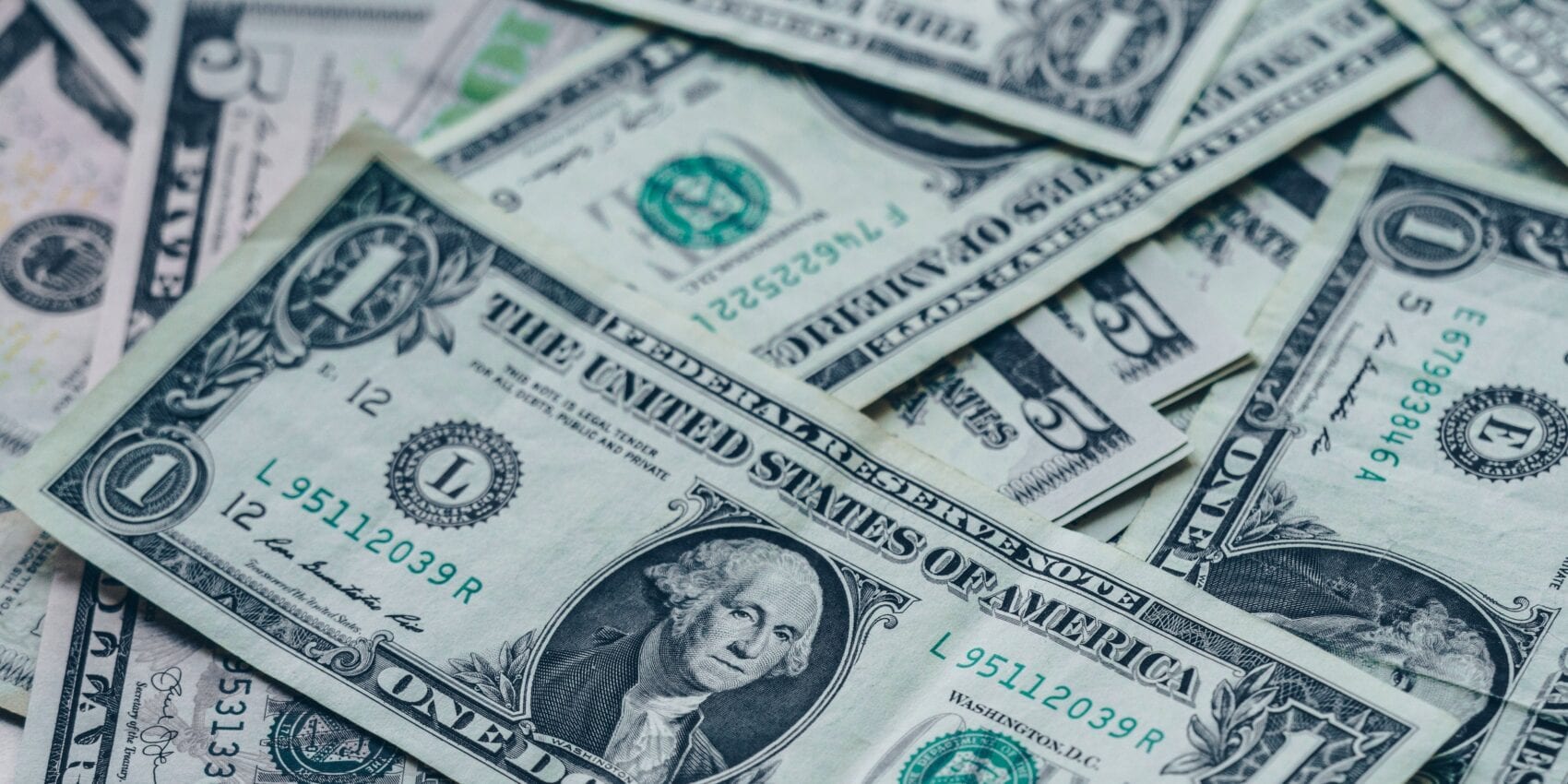 Close-up image of multiple U.S. one-dollar bills scattered and overlapping, showing American currency details and George Washington’s portrait.