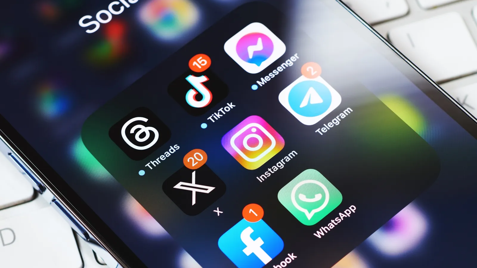Ecrã de smartphone em primeiro plano exibindo uma pasta de redes sociais com os ícones do Threads, TikTok, Messenger, X, Instagram, Telegram, Facebook e WhatsApp.