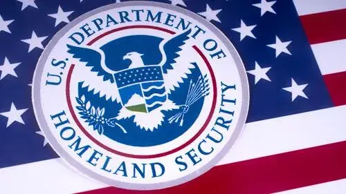 Selo do Departamento de Segurança Interna dos EUA (DHS) sobreposto à bandeira dos Estados Unidos.