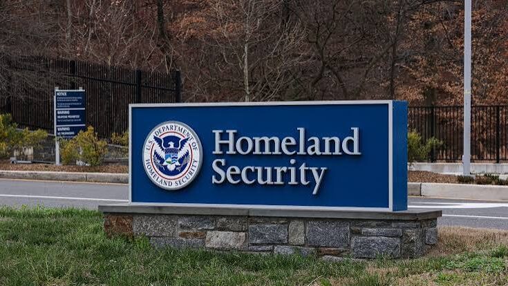 Large blue entrance sign for the U.S. Department of Homeland Security with official seal mounted on a stone base outside a facility.